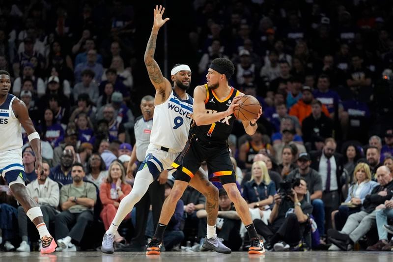 Phoenix Suns guard Devin Booker looks to pass as Minnesota Timberwolves guard Nickeil Alexander-Walker (9) defends during the first half of Game 3 of an NBA basketball first-round playoff series, Friday, April 26, 2024, in Phoenix. (AP Photo/Matt York)