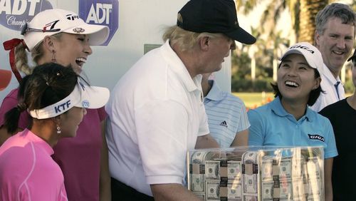 This Nov. 18, 2006 file photo shows Donald Trump, center, putting his hands on a box of money while posing for a photo with the eight golfers who qualified for the final round following the third round of the LPGA ADT Championship at the Trump International Golf Club in West Palm Beach, Fla. Also present, from left to right, are: Mi Hyun Kim, of South Korea, Natalie Gulbis and il Mi Chung, also of South Korea. The U.S. Women's Open will be played next week at a golf course in New Jersey owned by President Trump. The USGA awarded the site in 2012 and later came under pressure from women's groups and three Democratic U.S. senators to move the event because of Trump's comments about women and minorities. It's uncertain if the president will attend the tournament in Bedminster, New Jersey. (AP Photo/Lynne Sladky)