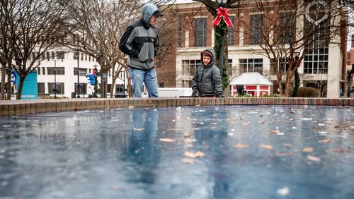 Bradley Thomas and his 5-year-old son, Briland, stand beside a frozen fountain on the Marietta Square on Monday, New Year’s Day. (Branden Camp / for the AJC)