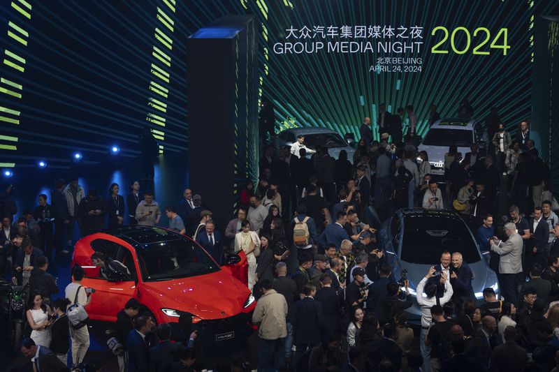 Attendees look at the cars shown to the media at an event held by the Volkswagen Group a day before the auto show in Beijing, Wednesday, April 24, 2024. The Volkswagen Group, which includes Audi and Porsche, plans to launch 40 new models in China over the next three years and to have a lineup of 30 EVs by 2030. (AP Photo/Ng Han Guan)