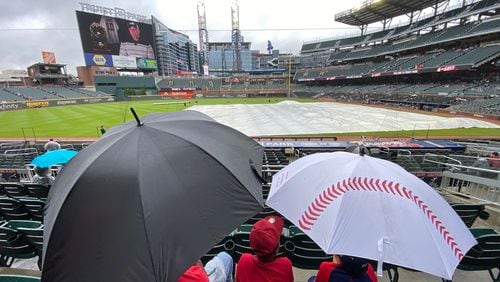 Fans take cover with umbrellas in the stands during a rain delay before the Braves' game against the Colorado Rockies was postponed Thursday at Truist Park. (Hyosub Shin / Hyosub.Shin@ajc.com)