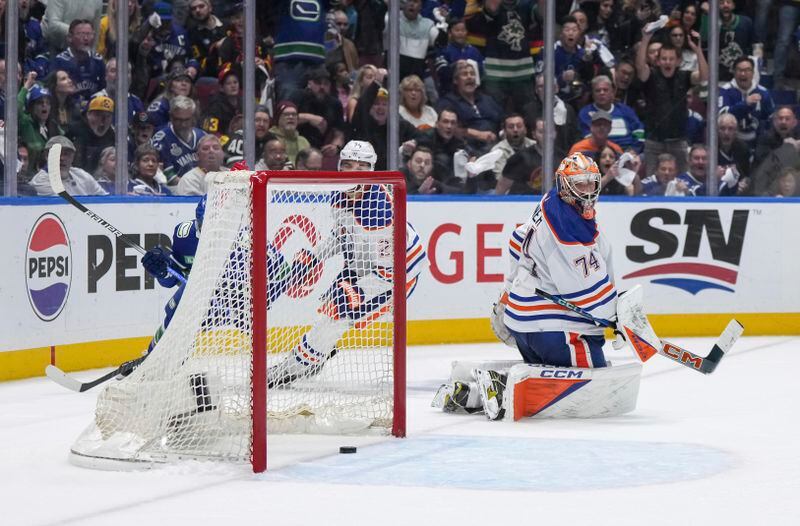 Edmonton Oilers goalie Stuart Skinner (74) looks back at the puck as it bounces out of the net after Vancouver Canucks' Conor Garland, hidden back left, scored during the third period of Game 1 of a second-round NHL hockey Stanley Cup playoffs series, Wednesday, May 8, 2024, in Vancouver, British Columbia. (Darryl Dyck/The Canadian Press via AP)
