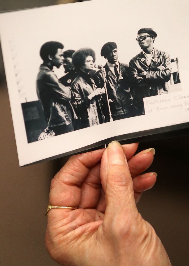 Kathleen Cleaver looks over a historical Black Panther photo taken in 1968 of  herself at the microphone during a “Free Huey Rally” along with Bobby Seal and George Murray at her Emory Law School office in November 2016 in Atlanta. Curtis Compton /ccompton@ajc.com