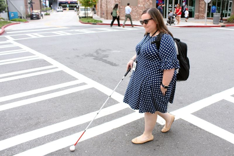 Katie Hearn crosses the street to go to her job with the Atlanta Braves’ social media department at SunTrust Park. Katie says she listens for vehicles whenever she goes to cross the street, but sometimes people around her will let her know that the street is clear. JENNA EASON / JENNA.EASON@COXINC.COM