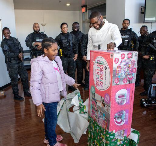 DeKalb County Sheriff’s Office holds the 16th annual Adopt-A-Family celebration on Tuesday, Dec 16, 2023. Alyah Pearson, 9, gets started opening one of several gifts that law enforcement officers bought for her.  (Jenni Girtman for The Atlanta Journal-Constitution)