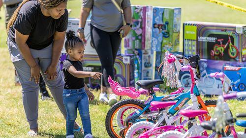 Porche Johnson helps her daughter Sanay Barry, 2,  pick out a new bike during the Sheriff's Office Saturday bike-a-thon in Atlanta on May 11, 2024.   (Steve Schaefer / AJC)