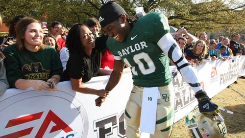 Heisman Trophy-winner and former Baylor quarterback Robert Griffin III is greeted by Holly Johnson on the Baylor campus, Monday, Feb. 27, 2012, in Waco, Texas, where he posed for photos for EA Sports NCAA Football 13 video game to be released in July. Video-game developer EA Sports is breaking back into the college football world 11 years after lawsuits over using players’ likeness without compensation froze the franchise. (Jerry Larson/Waco Tribune-Herald via AP)