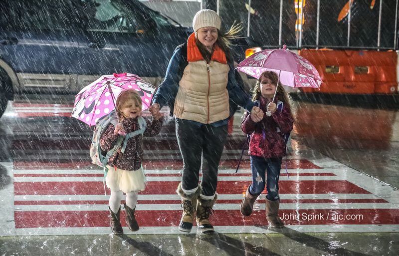 Katie Moghaizel and her daughters, 3-year-old Elsa (left) and 5-year-old Dori, brave the rain Thursday morning at the Hartsfield-Jackson International Airport domestic terminal, heading off to visit family for the holidays. JOHN SPINK / JSPINK@AJC.COM