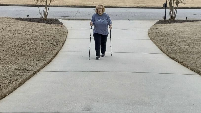 Stephanie Schroeder of McDonough taking a walk up her driveway. Because long COVID has wreaked havoc with her balance, she says she uses the walking sticks to steady herself. “Some days, I’m all right, but I can’t tell you which days I will feel good,” she said. “It’s all very frustrating because you know what you were capable of doing before.” (Contributed)