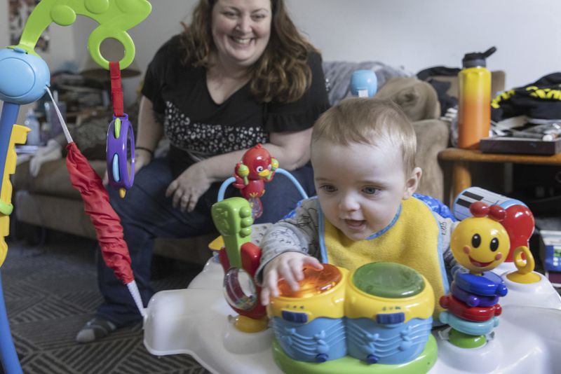 Nicole Slemp, a new mother of seven-month-old William, watches as her son plays in one of his favorite toys in their home Thursday, March 14, 2024 in Auburn, Wash.. Slemp recently quit her job because she and her husband couldn't find child care they could afford. Expensive, scarce child care is putting Puget Sound parents out of work. (Ellen M. Banner/The Seattle Times via AP)