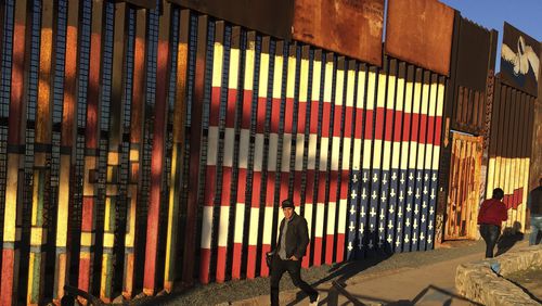 People pass graffiti along the border structure in Tijuana, Mexico, Wednesday, Jan. 25, 2017. President Donald Trump moved aggressively to tighten the nation's immigration controls Wednesday, signing executive actions to jumpstart construction of his promised U.S.-Mexico border wall and cut federal grants for immigrant-protecting "sanctuary cities." (AP Photo/Julie Watson)
