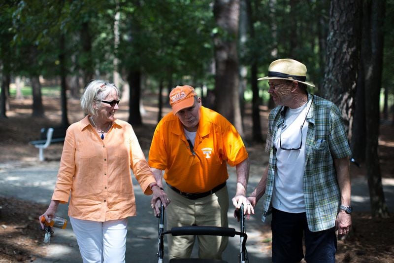 Walter Chadwick (center), who was a star running back at the University of Tennessee in the 1960s, walks with his friend and University of Tennessee alum Ellen Morrison (left) and former Wills High School football player Keith Miller in Laurel Park on Aug. 28, 2016, in Marietta. Chadwick was named head coach of Wills High School in 1971, but after he was on the job just two weeks, a Wells Fargo armored van slammed into his car, leaving Chadwick brain-damaged. Chadwick recently gathered with friends and former students, many of whom thought he was dead. BRANDEN CAMP / SPECIAL