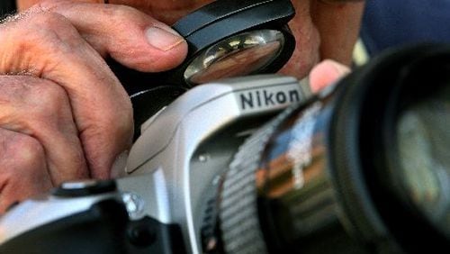 Though legally blind, Oraien Catledge had photographed Cabbagetown for more than two decades at the time of this 2006 photo in which he's shown using a magnifying glass to check the settings on his camera. CONTRIBUTED BY JOEY IVANSCO