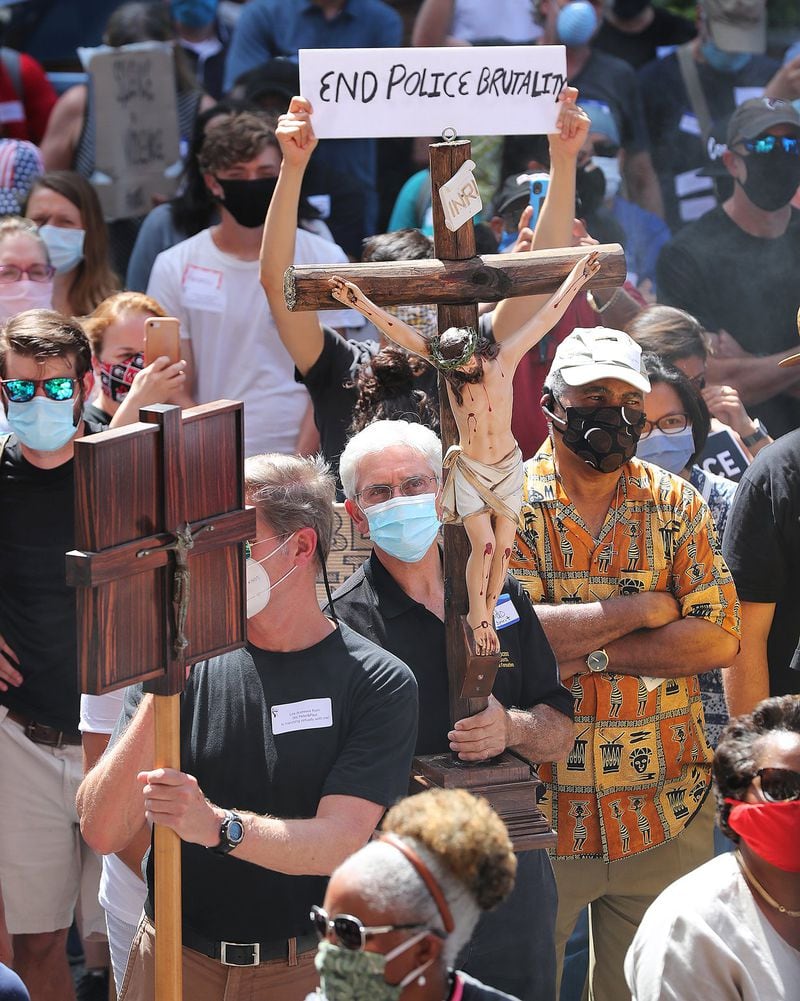 Orlando Caicedo (center) carries a cross while hundreds of Catholics march from the Catholic Shrine of the Immaculate Conception to Centennial Olympic Park in Atlanta on Thursday, June 11, 2020, demanding justice and an end to police brutality. (credit: Curtis Compton / ccompton@ajc.com)