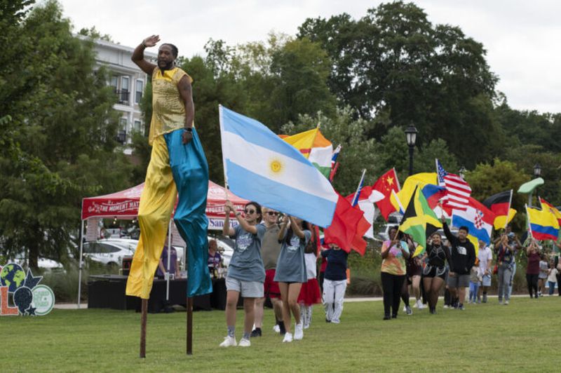 A stilt walker leads a parade of flag-bearers for the opening of “Around the World in the DTL” in Lawrenceville, Ga. September 9, 2022. Volunteers from the audience held up flags of several countries from all over the world. (Kendra A. Ransum/Fresh Take Georgia)