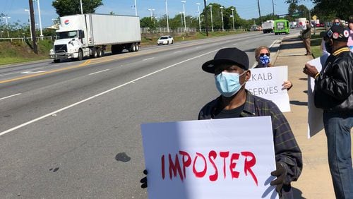 A protester holds a sign that reads "imposter" in red capital  letters outside the DeKalb County School District headquarters on Mountain Industrial Boulevard in Stone Mountain on Friday, May 1, 2020. (MARLON A. WALKER/marlon.walker@ajc.com)