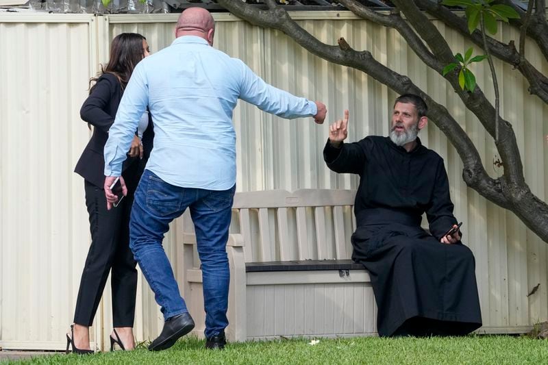 Father Daniel Kochou, right, gestures as he speaks with people, across the road from the Christ the Good Shepherd church in suburban Wakely in western Sydney, Australia, Tuesday, April 16, 2024. Australian police say a knife attack in Sydney that wounded a bishop and a priest during a church service as horrified worshippers watched online and in person, and sparked a riot was an act of terrorism. (AP Photo/Mark Baker)