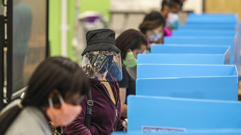 C.K. Hoffler (center) wore a face shield as she voted at Cross Keys High School located at 1626 N Druid Hills Rd NE in DeKalb County where volunteers passed out water bottles to a crowd of 100 voters lined up for hours outside the building. JOHN SPINK/JSPINK@AJC.COM