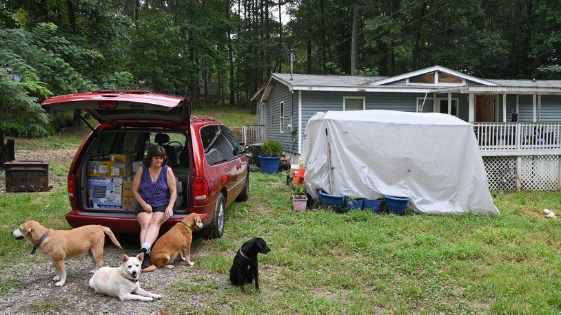 Kathy Poland-Jones plays with her dogs as she sits on the back of her van where she has loaded up boxes for moving out at their home in Canton on Tuesday. Poland-Jones, 65, had lost her full-time job and took part-time work, but she hasn’t been able to keep up her payments. She got an eviction notice in June. “Nobody would rent to me before,” she said. “I have no idea where to go.” (Hyosub Shin / Hyosub.Shin@ajc.com)