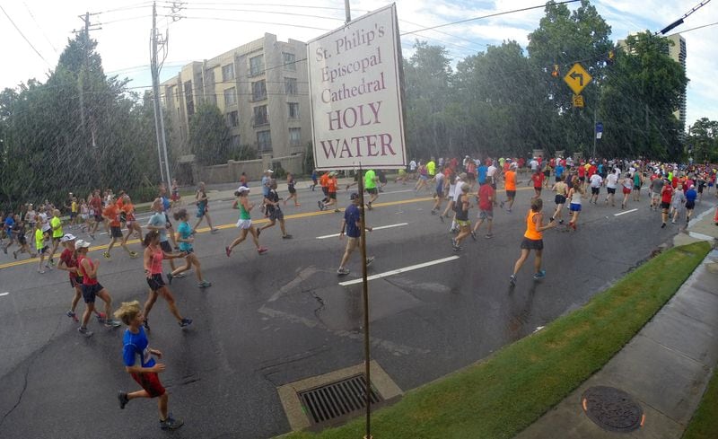 Some runners go for a quick blessing under the holy water sprinkler at the Cathedral of St. Philip as they make their way down Peachtree Road in Buckhead during the AJC Peachtree Road Race on July 4, 2014. AJC FILE PHOTO