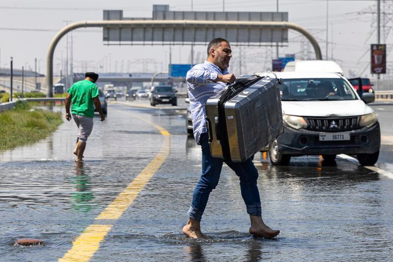A man carries luggage through floodwater caused by heavy rain while waiting for transportation on Sheikh Zayed Road highway in Dubai, United Arab Emirates, Thursday, April 18, 2024. The United Arab Emirates attempted to dry out Thursday from the heaviest rain the desert nation has ever recorded, a deluge that flooded out Dubai International Airport and disrupted flights through the world's busiest airfield for international travel. (AP Photo/Christopher Pike)