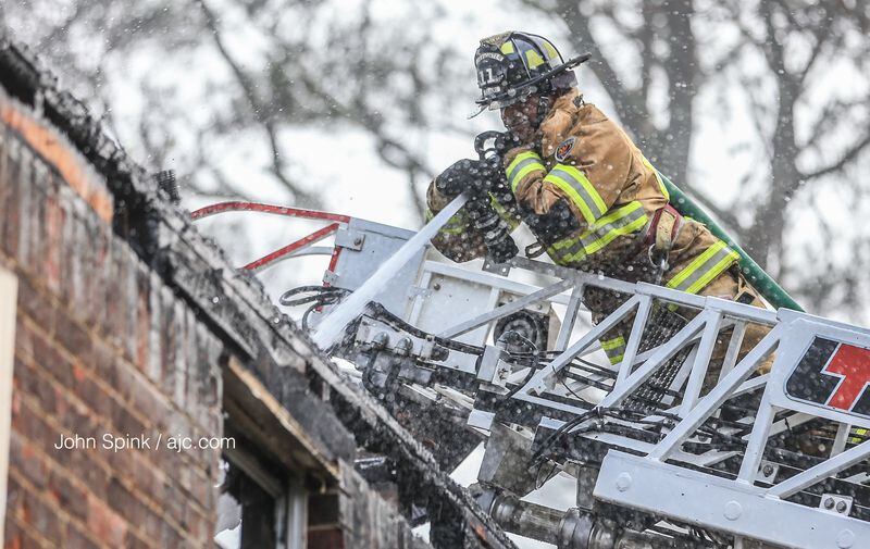 Fulton County firefighter John Henderson hits hot spots at the Westwood Glen  Apartments, where two residents were burned. JOHN SPINK / JSPINK@AJC.COM