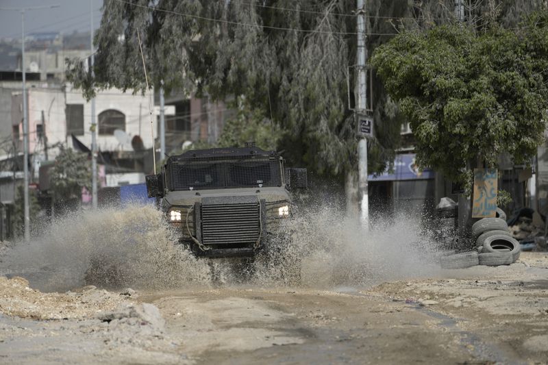 An Israeli military vehicle drives through water during a military operation in the nearby Nur Shams refugee camp, near the West Bank town of Tulkarem, Saturday, April 20, 2024. The raid killed at least four Palestinians, including three militants, according to the Israeli military, Palestinian health officials and the Islamic Jihad militant group. (AP Photo/Majdi Mohammed)