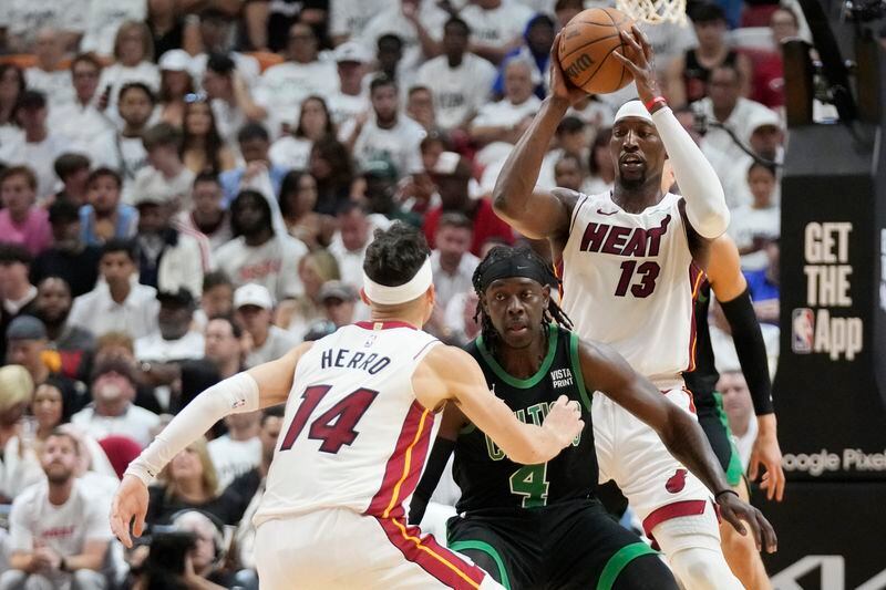 Miami Heat center Bam Adebayo (13) attempts to pass to guard Tyler Herro (14) past Boston Celtics guard Jrue Holiday (4) during the first half of Game 3 of an NBA basketball first-round playoff series, Saturday, April 27, 2024, in Miami. (AP Photo/Wilfredo Lee)