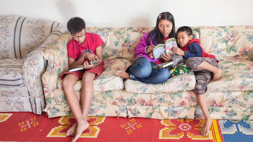 Ram, En Kawli and Bawi reading while seated on the couch in the family living room.  They understand the importance of reading for continued learning of English.
