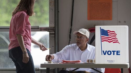Toni Kuhn, left, hands her voter card to Birdel Jackson III at Alpharetta Fire Station 82 during an election in April. (DAVID BARNES / DAVID.BARNES@AJC.COM)
