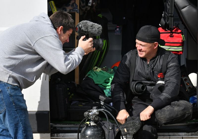 A fellow scuba diver Britain Lockhart (left) films as Jeremy Sides prepares to dive in the Chattahoochee River for his YouTube channel, Exploring with Nug. Sides first began searching creeks and rivers for gold nuggets and Civil War artifacts, but has become adept at locating missing persons and solving cold cases.  (Hyosub Shin / Hyosub.Shin@ajc.com)