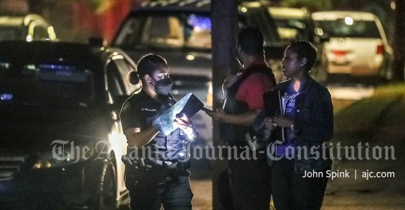 An Atlanta police officer (left) speaks with investigators from the Fulton County District Attorney's Office on the scene of a deadly shooting Thursday on Beatie Avenue in southwest Atlanta.