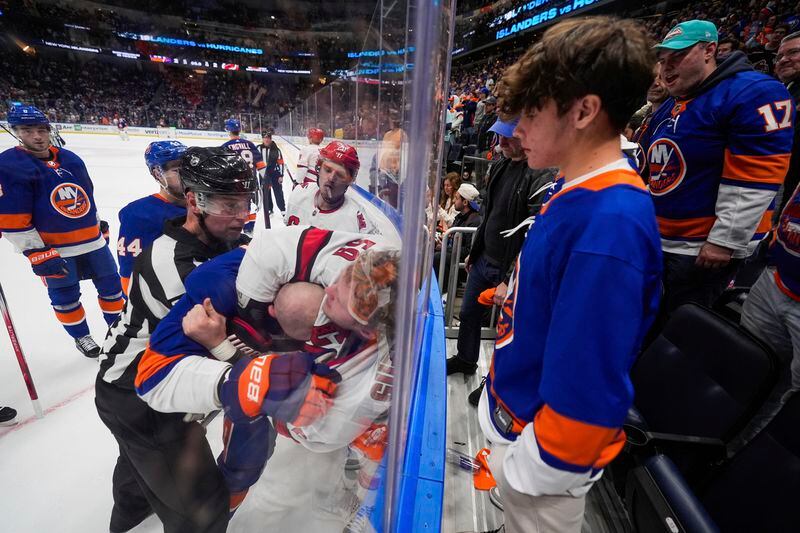 Referee Eric Furlatt (27) attempts to separate New York Islanders' Adam Pelech, center, and Carolina Hurricanes' Jake Guentzel, right, during the overtime period of Game 4 of an NHL hockey Stanley Cup first-round playoff series Saturday, April 27, 2024, in Elmont, N.Y. (AP Photo/Frank Franklin II)