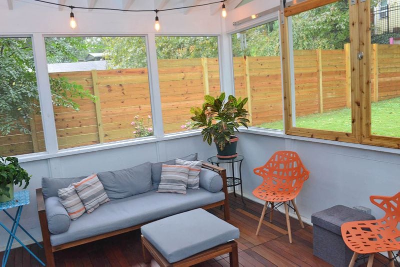 The enclosed back porch was added by Chris Erickson during the renovation. The gray-and-orange sofa is from Bellacor.com and matches the orange chairs from Amazon. The round glass side table is from Ikea. The flooring is Brazilian ipe wood.