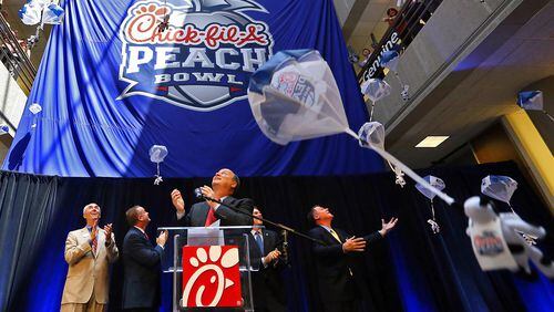 Steve Robinson (from left), Chick-fil-A executive vice president; Michael Kelly, College Football Playoff executive; Gary Stokan, bowl president; Rob Temple, ESPN vice president; and Burke Magnus, ESPN senior vice president, look up as the bowl’s new name Chick-fil-A Peach Bowl logo is unveiled while parachuting cows drop from the ceiling Monday, April 21, 2014, in Atlanta. CURTIS COMPTON / AJC file