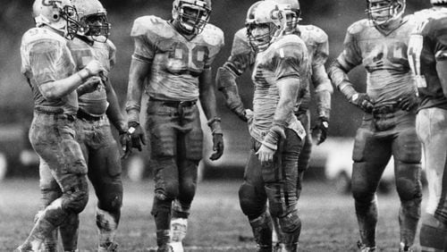 Ted Roof (center), Pat Swilling (99) and other Georgia Tech defensive players are soaked in mud during a game against Duke in 1985. Incoming Georgia Tech freshman Bruce Jordan-Swilling and Tre Swilling give Roof, now Tech’s defensive coordinator, a large amount of credit for their choosing to become Yellow Jackets. (Andy Sharp / AJC file)