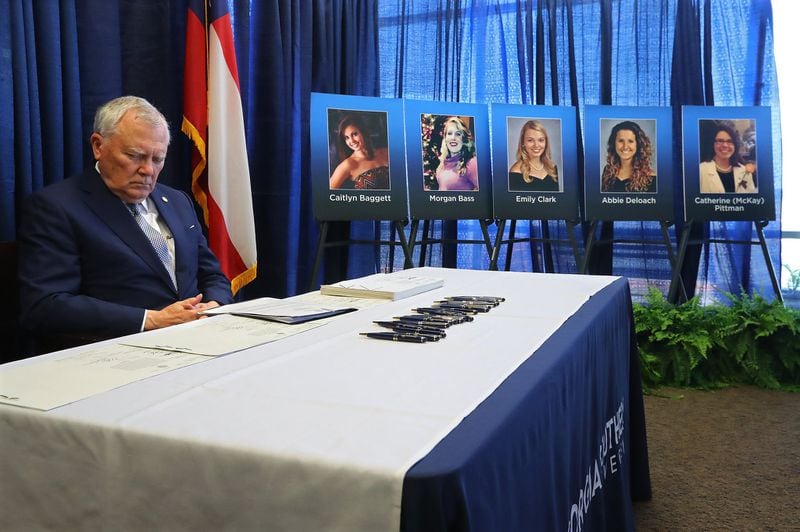 Governor Nathan Deal bows his head for a somber moment before signing HB 673 prohibiting Georgia motorists from handling their cell phones while driving. The governor is sitting beside the portraits of five nursing students who died when they were struck by a semi on nearby I-16 in 2015. Curtis Compton/ccompton@ajc.com