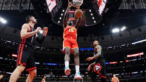 Atlanta Hawks center Clint Capela, center, hangs from the rim after dunking as Chicago Bulls center Nikola Vucevic, left, and forward DeMar DeRozan look on during the first half of an NBA basketball game in Chicago, Monday, April 1, 2024. (AP Photo/Nam Y. Huh)