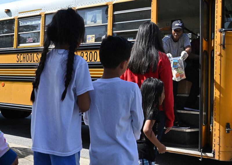 Jocelyn Zanzala (background), school bus driver, delivers a free meal to students at their school bus stop on Friday, March 20, 2020. Gwinnett County Schools offers meal pickup at 68 sites and bus stops near the schools from 11 a.m. to 1 p.m. for children 18 and under.