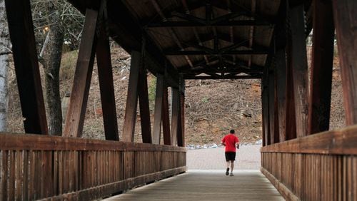 A runner crosses the Vickery Creek covered pedestrian bridge at Roswell’s Old Mill Park. AJC FILE