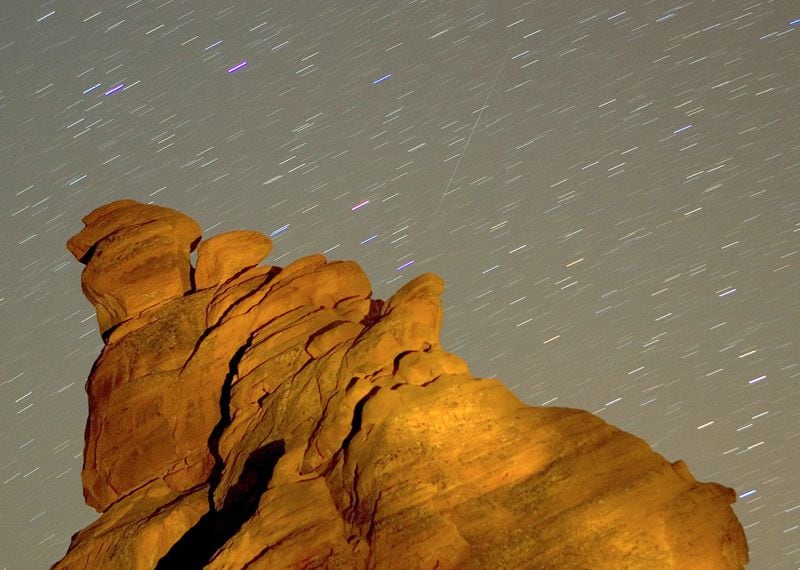 VALLEY OF FIRE STATE PARK, NV - DECEMBER 14: A Geminid meteor streaks diagonally across the sky against a field of star trails over one of the peaks of the Seven Sisters rock formation early December 14, 2007 in the Valley of Fire State Park in Nevada. The meteor display, known as the Geminid meteor shower because it appears to radiate from near the star Castor in the constellation Gemini, is thought to be the result of debris cast off from an asteroid-like object called 3200 Phaethon. The shower is visible every December. (Photo by Ethan Miller/Getty Images)