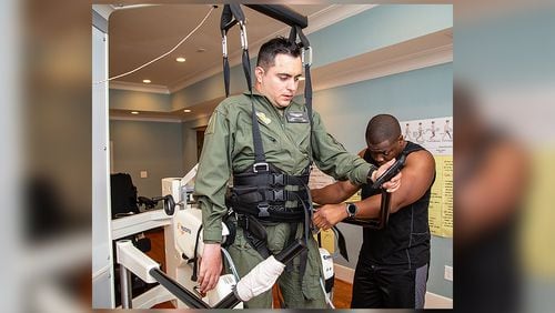 Ignacio Montoyo (left) gets help from Andre Ajayi preparing him to work out on a "Lokomat," a robot assisted locomotor training orthosis, in Atlanta on Monday August 12th, 2019. He was paralyzed in an accident while a student at Georgia Tech but persevered to get his degree and now works to improve the mobility of the paralyzed. (Photo by Phil Skinner)
