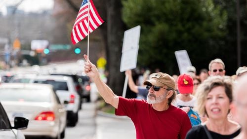 A marcher waves an American flag to passing traffic as car horns blare in support of the march, Monday, Feb. 20, 2017. (Cory Hancock for The AJC)