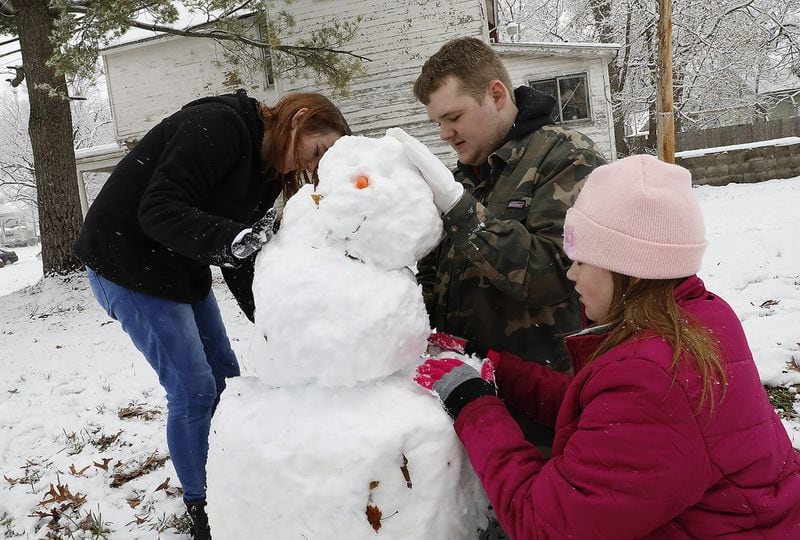 Andrew Davis and his sisters Brook, left, and Kyla make the first snowman of the season along Center Street in Springfield Tuesday. Bill Lackey/Staff