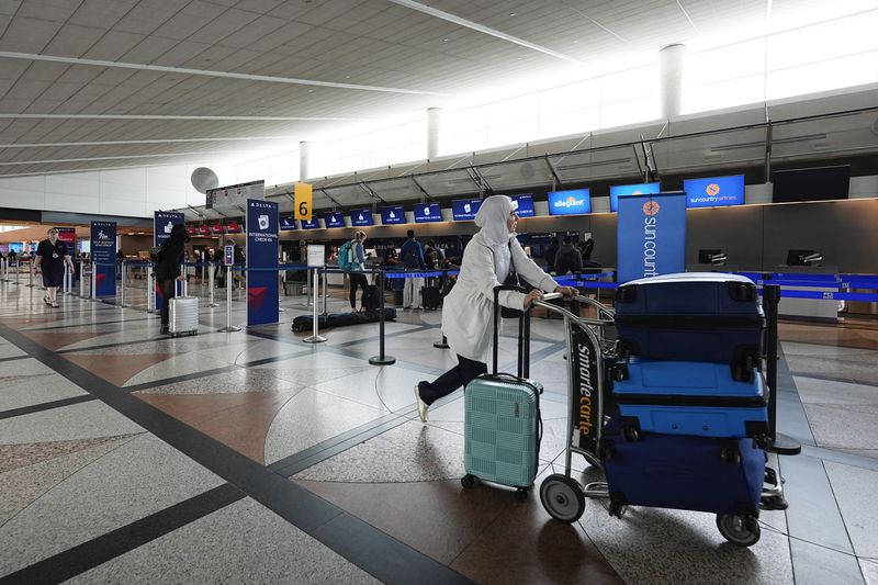 A traveler pushes a cart topped with baggage to the check-in counter for Lufthansa Airlines Tuesday, April 16, 2024, in Denver International Airport in Denver. (AP Photo/David Zalubowski)