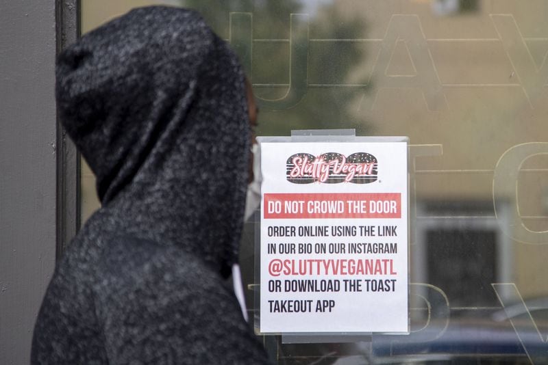 A masked customer waits for her food order while standing in line at the Slutty Vegan ATL restaurant, located at 1542 Ralph David Abernathy Boulevard SW, in Atlanta's Westview community, Thursday, April 30, 2020. (ALYSSA POINTER / ALYSSA.POINTER@AJC.COM)