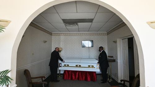 Garry Duty, left, and Deric Thomas, both funeral home staff, place a casket in a viewing room at Dudley Funeral Home in Dublin earlier this month. In August and September of 2020, the funeral home was handling two or three services a day, said Carl Pearson, director of client services. It usually does five or six a week. (Hyosub Shin / Hyosub.Shin@ajc.com)