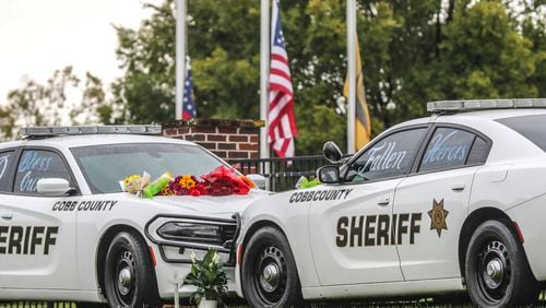 September 12, 2022 Atlanta: A memorial of two patrol cars parked with flowers and notes affixed against a backdrop of flags were lowered to half-staff at the Cobb County Sheriff's Office Adult Detention Center on Monday, Sept. 12, 2022 located at 1825 County Services Parkway in Marietta served as a reminder of the tragedy last week of two Cobb County deputies killed in the line of duty. (John Spink / John.Spink@ajc.com)