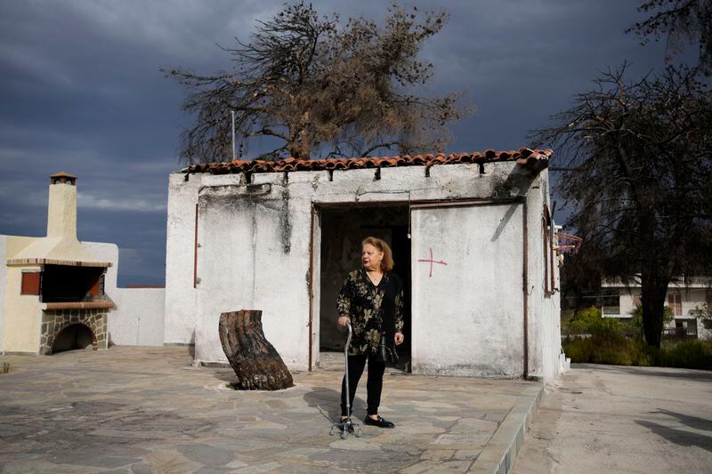 Retiree Chrysoula Renieri, 73, stands outside her house which was burned in July 2023 during a wildfire, in Loutraki, about 82 kilometres (51 miles) west of Athens, Greece, Thursday, April 25, 2024. Greece's fire season officially starts on May 1 but dozens of fires have already been put out over the past month after temperatures began hitting 30 degrees Celsius (86 degrees Fahrenheit) in late March. This year, Greece is doubling the number of firefighters in specialized units to some 1,300, adopting tactics from the United States to try and outflank fires with airborne units scrambled to build breaks in the predicted path of the flames. (AP Photo/Thanassis Stavrakis)