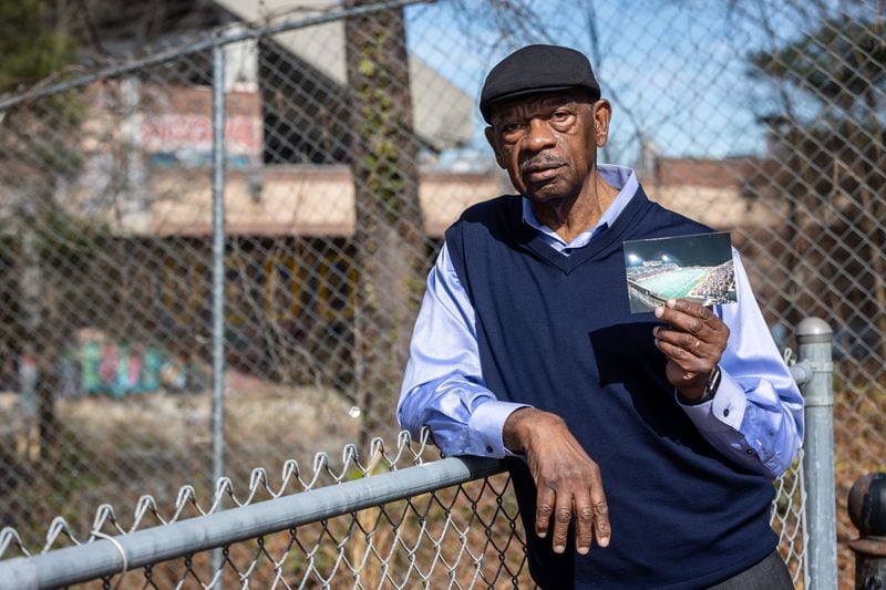 Coach Greg Thompson holds a photo of the Alonzo Herndon Stadium while standing outside the now-shuttered facility that has been abandoned since 2014.  (Steve Schaefer/steve.schaefer@ajc.com)